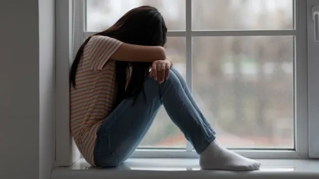 scared young person sitting on a windowsill