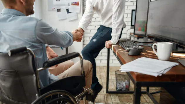 Wheelchair user working in an office talking to a colleague