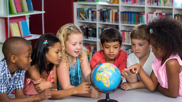 schoolchildren looking at a globe, pointing out different countries 