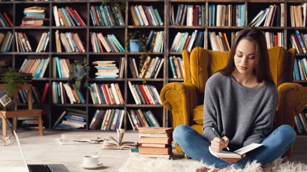 Young woman writer in library at home creative occupation sitting writing notes