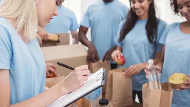 Group of volunteers working with donate food, team leader checking list in clipboard