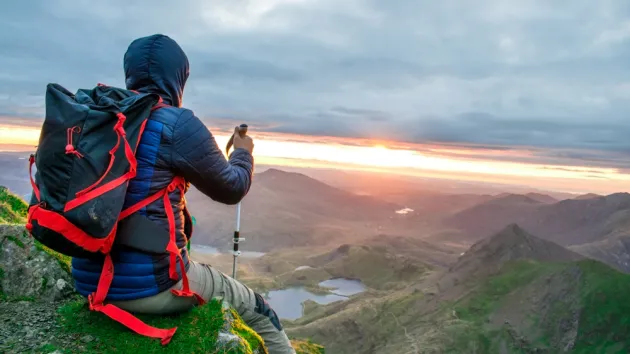  male hiker with backpack relaxing and looking at the beauty of green landscape nature in morning sunrise on top of Wyddfa