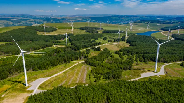 Aerial drone view of turbines at a large onshore windfarm on a green hillside (Pen y Cymoedd, Wales)