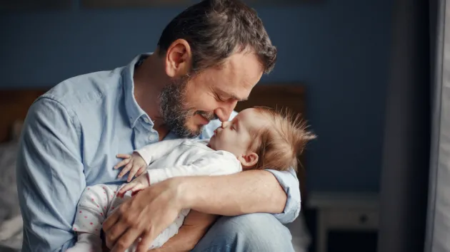 Middle age father kissing sleeping newborn baby girl. 