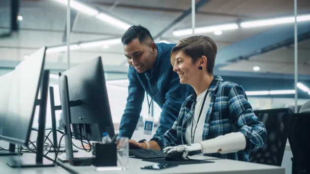 Project Manager Talks with Happy Woman with Disability with Prosthetic Arm to Work on Desktop Computer