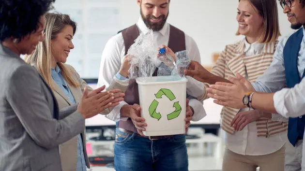 A group of employees in a pleasant atmosphere in the office ,collecting plastic bottles in the recycling bin. 