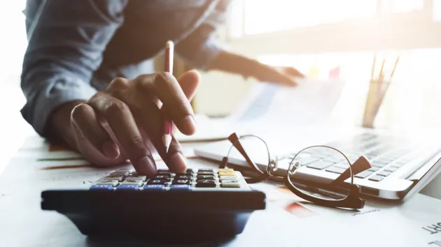 Close up of businessman or accountant hand holding pen working on calculator to calculate business data, accountancy document and laptop computer at office, business concept