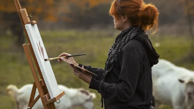 Woman painting - outdoors in a field of cows