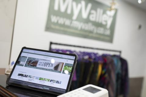 laptop open with the My Valley website up on screen and the business sign and clothes rail in the background