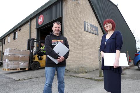 Man and woman stood in front of warehouse entrance holding laptops under their arms