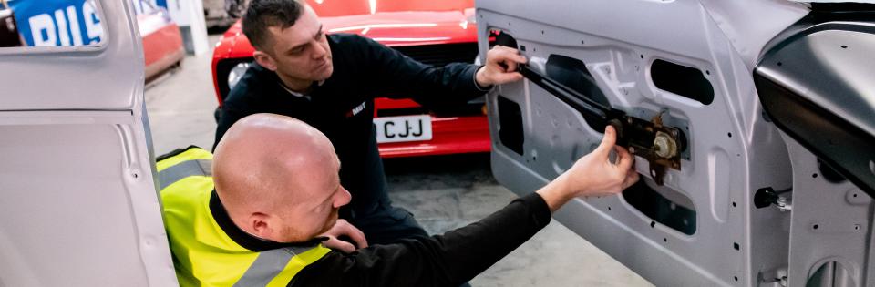 Two white men fix a part to a car door