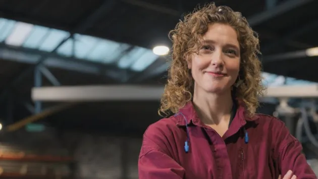 Woman with arms crossed and factory in the background
