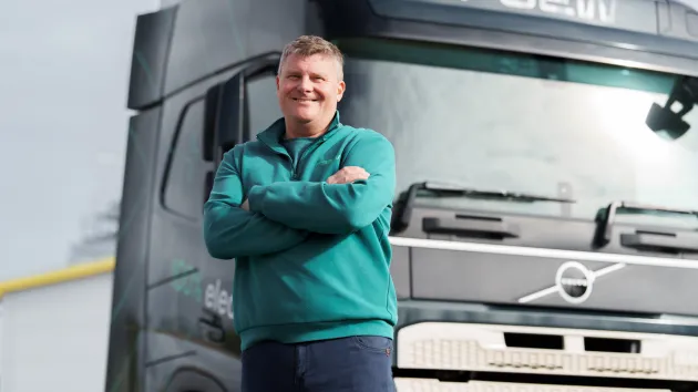 A man leaning against an electric truck with his arms crossed 