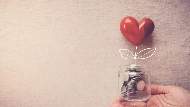 Hand holding a jar of coins and a red heart shape