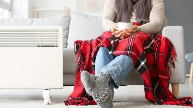 person wearing a scarf, covered by a blanket sitting close to a radiator