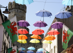 Some of the many umbrellas and Welsh flags hanging in Palace Street in Caernarfon in North Wales. One of the towers of Caernarfon Castle can be seen in the background.