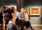  A tourist visits the sights of the Museum in a medical mask. People and pictures in the background. The concept of a viral pandemic and maintaining distance