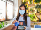 Waitress holding credit card reader machine and wearing protective face mask with client holding credit card. 