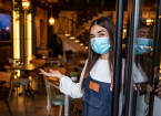 Woman wearing mask standing with open sign board on glass door in coffee shop and restaurant after coronavirus lockdown