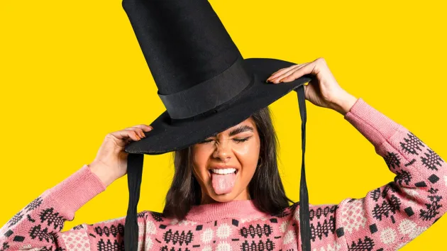 Woman wearing a tall Welsh hat and pink traditional Welsh jumper on a yellow background. 