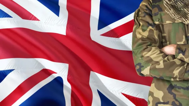 Crossed arms British soldier with national waving flag on background - United Kingdom Military theme.