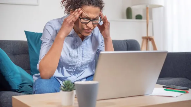 stressed female looking at a laptop, victim of fraud.