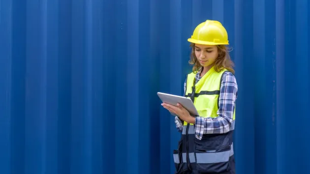 Woman stood by a shipping container looking at a digital tablet 