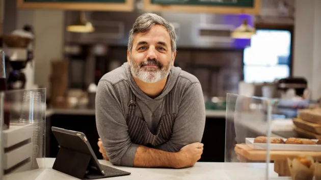 Male cafe owner, leaning on serving counter 