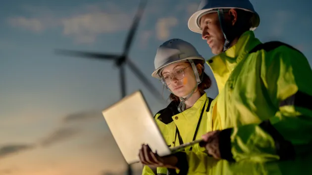 Engineers analysing smart grid data via laptop at onshore wind farm.