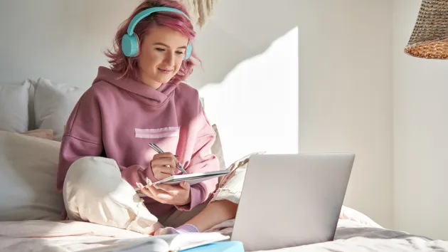  teen girl school student with pink hair wear headphone write notes watching video online webinar