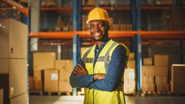 Happy Professional Worker Wearing Safety Vest and Hard Hat Smiling with Crossed Arms on Camera.