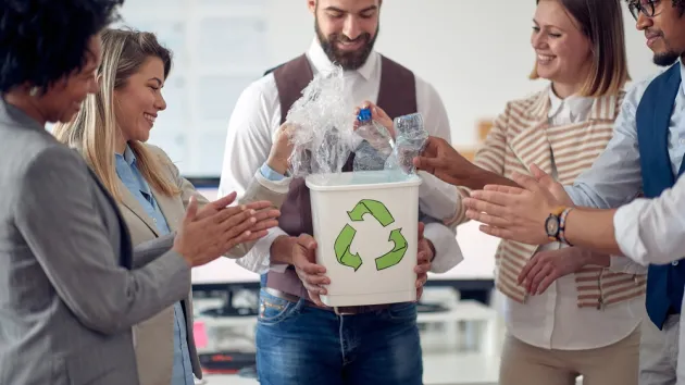 A group of employees in a pleasant atmosphere in the office, collecting plastic bottles in the recycling bin. 