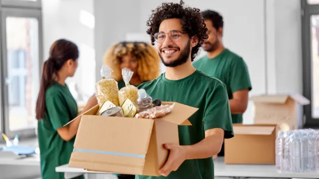 charity, donation and volunteering concept - happy smiling male volunteer with food in box and international group of people at distribution or refugee assistance centre