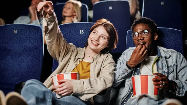 Young woman and her friend spending time together at cinema watching movie and eating popcorn