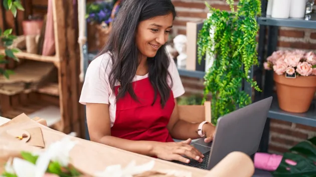  woman florist smiling confident using laptop at flower shop