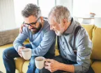 Grandfather and grandson sitting on a settee drinking coffee 