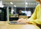 person in an office wearing a yellow jumper using a laptop 