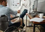 Wheelchair user working in an office talking to a colleague