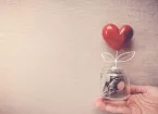 Hand holding a jar of coins and a red heart shape