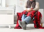 person wearing a scarf, covered by a blanket sitting close to a radiator