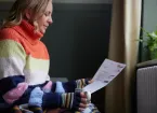 person trying to keep warm by a radiator looking at a utility bill 