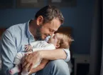 Middle age father kissing sleeping newborn baby girl. 