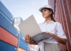 manager or engineer worker in casual suit standing in shipping container yard holding laptop