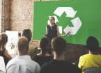 People listening to a speaker, recycling symbol in the background