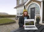 lady sitting in front of a farmhouse on the coast with a laptop displaying her website