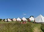 Bell tents lined up in a field and clear blue skies