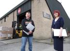 Man and woman standing in front of warehouse entrance holding laptops under their arms