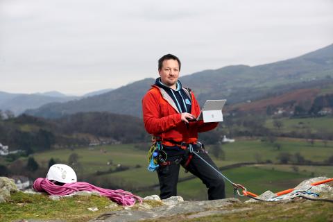 owner of climb wales Glyn holding laptop on mountainside