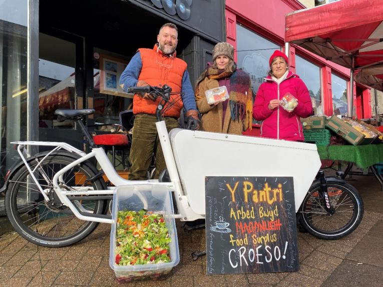 Tyfu Dyfi's James Cass, and Gabi Ashton and Maggie Day from Y Pantri at the Taj Mahal Community Hub hand over food to a Criw Compostio electric cargo bike.
