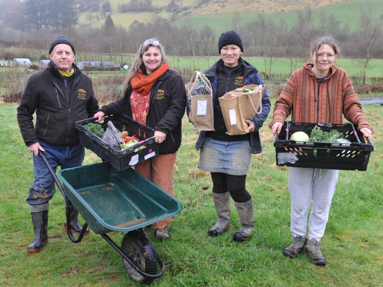 image showing 4 growers holding veg boxes with a wheelbarrow